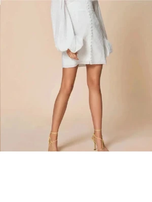 Vit kort klänning med puffärmar - Superfin vit kort klänning med v-ringning, puffiga långärmar och knappar framtill. Klänningen har en feminin passform och är perfekt för dig som vill sticka ut. Snygg och trendig design som passar till många tillfällen.