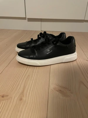 Svarta sneakers från Gant - Stilrena svarta sneakers från Gant med vit sula och klassisk låg profil. Skorna har svarta skosnören och Gant-logga på sidan. Tillverkade i skinn för en clean och modern look.använda 3 gånger storlek 43 ,28.6 cm 