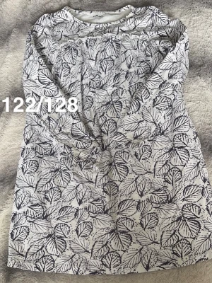 Vitt nattlinne med svart lövmönster - Nattlinne i vitt med svart lövmönster över hela plagget. Långärmad modell med rund halsringning och avslappnad passform. perfekt för mysiga kvällar.🌸 Fint använt skick. Storlek 122/128 