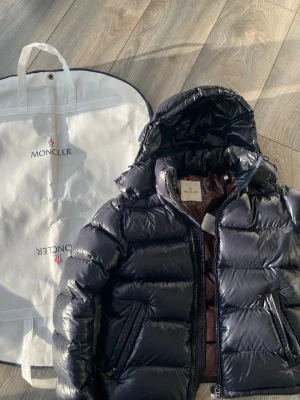 Navy blue Moncler maya - Snygg mörkblå pufferjacka från Moncler med glansig finish och huva. Köpt före denna vinter så endast använd nu under vintern inga defekter eller liknande storlek 2. ENDAST SERIÖSA KÖPARE!!