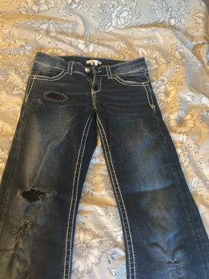 Mörkblå jeans med slitningar - Snygga mörkblå jeans med kontrastsömmar och slitna detaljer på benen. Bakfickan har en broderad design som ger extra attityd. Perfekta för dig som gillar en avslappnad och trendig stil.