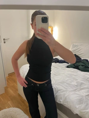 Svart ärmlös halterneck-top - Säljer en svart, tight halterneck-top med hög hals och ärmlös design. Perfekt att styla med jeans eller kjol för en trendig look. Toppen har en slimmad passform och är gjord i ett stretchigt material som sitter snyggt på kroppen.