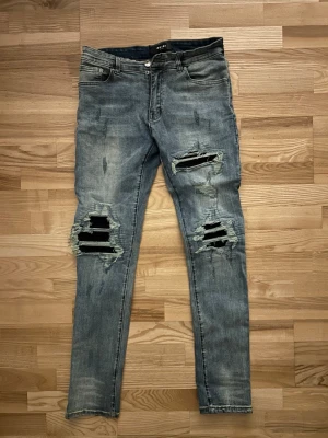 Blå slitna skinny jeans från Amiri - Säljer ett par blå skinny jeans från Amiri med kraftiga slitningar och hål på båda benen. Jeansen har klassisk femficksmodell, låg midja och är tillverkade i denim med stretch. Perfekta för en trendig och avslappnad streetstyle-look.