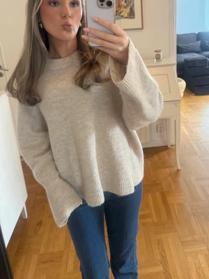 Beige oversized stickad tröja - Mysig beige stickad tröja med oversized passform och långa ärmar. Tröjan har ribbstickade muddar vid ärmslut och nederkant. Perfekt för lager-på-lager och enkel att styla med jeans eller kjol.