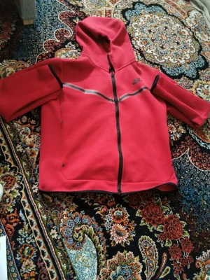 Röd hoodie från Nike med dragkedja - Snygg röd hoodie från Nike med hel dragkedja framtill och huva. Hoodien har svarta detaljer längs dragkedjan och över bröstet samt två sidofickor. Tillverkad i mjukt material som passar perfekt för chill eller träning.