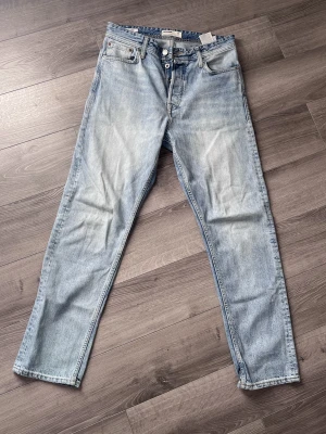 Ljusblå loose fit jeans LOOSE/CHRIS - Säljer ett par ljusblå loose fit jeans med raka ben och klassisk femficksdesign. Jeansen har en avslappnad passform och snygga slitningar framtill. Perfekta för en chill och trendig look.