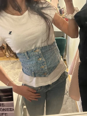 Denim korsett med knappar - Trendig korsettopp i ljusblå denim med knappar framtill och markerad midja. Perfekt över en t-shirt eller en skjorta! strechig🫶🏽