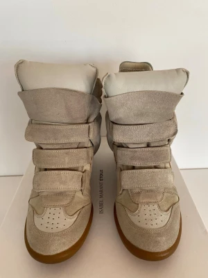 Beige höga sneakers Isabel Marant - Snygga höga sneakers från Isabel Marant i beige mocka och läder. Skorna har flera kardborreband, perforerad tå och en chunky gummisula. Perfekt för dig som vill ha en unik och trendig look med streetkänsla.