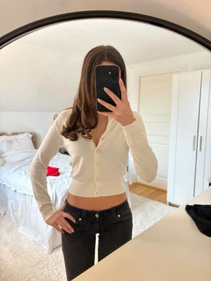 Vit cropped kofta från H&M - Snygg gräddvit cropped kofta från H&M med rund halsringning och knappar framtill. Långärmad modell i mjukt, tunt material som passar perfekt till jeans eller kjol. Enkel och stilren design som är lätt att matcha.