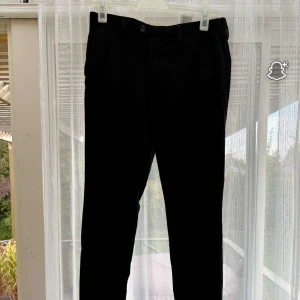 Svarta slim kostymbyxor Slim Marco - Svarta kostymbyxor från Jack & Jones, modell Slim Marco. Byxorna har slim passform, bälteshällor och knappstängning fram. Snygg och stilren look som funkar till skjorta eller t-shirt. Materialet är mjukt och känns bekvämt mot huden.