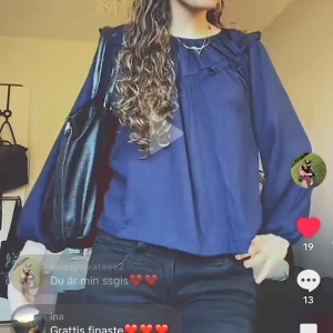 Mörkblå långärmad blus - Supersöt mörkblå blus med volangdetaljer längs ringningen och långa puffiga ärmar med resår vid handlederna. Blusen har en lös passform och är tillverkad i ett mjukt, lätt material som känns skönt mot huden. Perfekt för dig som gillar en romantisk och chill stil.