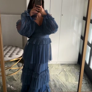 Blå långklänning med volanger och puffärm - Säljer en drömmig blå långklänning med flera lager volanger och puffiga långärmar i transparent tyg. Klänningen har v-ringning, markerad midja och öppen rygg. Perfekt för dig som vill sticka ut med en romantisk och flowy look.