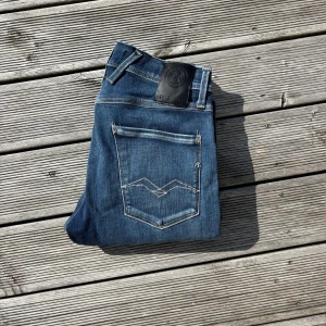 Replay Anbass blå jeans slim fit - Snygga blå jeans från Replay, modell Anbass. Jeansen har en klassisk femficksdesign, smal passform och subtila slitningar. Tydliga Replay-detaljer vid fickan och bakficka med dekorativ söm. Perfekta för dig som gillar en modern och stilren look. W27 L32