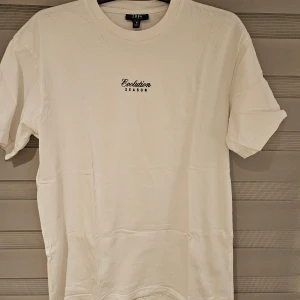 Vit t-shirt med färgglada vingar från Smog - Vit t-shirt från Smog i relaxed fit med trycket 'Evolution Season' fram och ett stort, färgglatt vingmotiv i blått och grönt på ryggen. Rund hals och korta ärmar. Tillverkad i mjuk bomull, perfekt för dig som gillar unika prints och streetstyle.