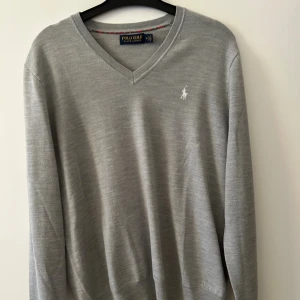 Stickad Ralph Lauren tröja - V ringad grå stickad Ralph Lauren tröja. Aldrig använd, men har en liten defekt. Det var ett hål i produkten när jag själv köpte den, men det är lagat hos en skräddare så syns verkligen inte. Skicket är därför 9/10. Vet inte riktigt nypris då jag fått tröjan i present, mitt pris är dock endast 500 kr. Perfekt stickad tröja inför hösten. Vid frågor eller funderingar skriv. 