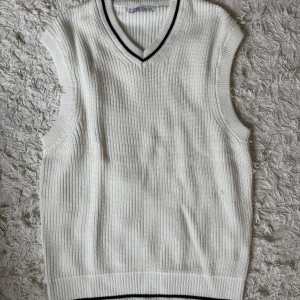 Vit stickad väst från Zara - Säljer en vit stickad väst från Zara i storlek M. Västen har v-ringad hals med svarta ränder och ribbade kanter. Den är gjord i ett grovt stickat material.