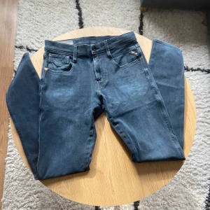 Mörkblå/grå Replay - Snygga mörkblå jeans från Replay med klassisk femficksdesign och diskret Replay-logga på fickan👖Jeansen har raka ben och normal passform, tillverkade i mjukt denimtyg som sitter skönt hela dagen🙌 Perfekta för dig som gillar stilrena och tidlösa jeans⏱️  Jeansen är i Anbass modell och har hyperflex material🪢 De har storlek W28 L32📐  Vid frågor: Meddela oss!📩