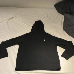 Svart hoodie från Polo Ralph Lauren M - Svart hoodie från Polo Ralph Lauren i storlek M. Klassisk design med huva, känguruficka och den ikoniska vita broderade loggan på bröstet. Tillverkad i mjuk bomull, perfekt för chill dagar eller när du vill ha en clean streetstyle.