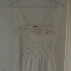 Vit topp med smock - Säljer en vit topp med smock upptill och tunna axelband. Toppen  har en luftig och lätt känsla, perfekt för varma dagar. Den är ärmlös och har en mjuk, böljande nederdel.Otroligt fin., vet inte storlek men tror S/M!
