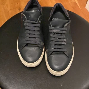 Blåa sneakers från Axel Arigato - Stilrena blåa sneakers från Axel Arigato med vit sula och klassisk snörning. Skorna är i skinn och har en låg profil med rund tå. Perfekta för dig som gillar minimalistisk och clean design.