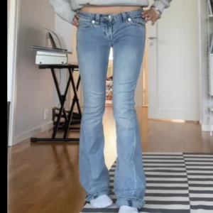 Ljusblå True Religion bootcut jeans - Säljer ett par ljusblå jeans från True Religion med bootcut passform och snygga detaljerade bakfickor med knappar. Jag har sytt om sömmen där bak till en ljusrosa. Jeansen har låg midja och klassisk femficksdesign. Perfekta för dig som gillar en avslappnad men trendig look.