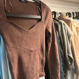 Brun ribbad topp från Gina Tricot - Brun långärmad topp från Gina Tricot med snygg v-ringad halsringning och ribbad struktur. Modellen är figurnära och har små slitsar vid ärmslut och nederkant. Perfekt för dig som gillar en enkel men trendig look. (Lite nopprig)