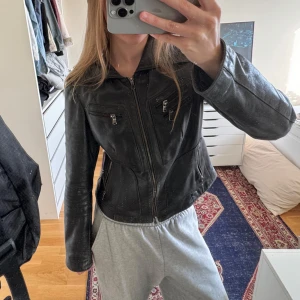 Svart skinnjacka med dragkedjor - Snygg svart skinnjacka med markerad krage och flera dragkedjor framtill. Superbra skick, inga tecken på användning. 