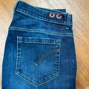 Dondup George - Snygga blå jeans från Dondup, modell George med skinny fit. Klassisk femficksdesign, kontrastsömmar och läderpatch bak i midjan. Jeansen är tillverkade i stretchig denim för en tight och bekväm passform. Lappen är avklippt av förra ägaren men storleken är 48cm midja och 1 meter yttre längd