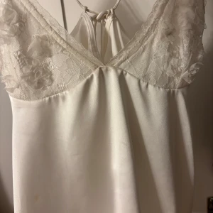 Vit satin linne från Zara - Supersöt vit linne från Zara i satin med spetsdetaljer och blommor upptill. Har bara använt den tre gånger så den är nästan ny.