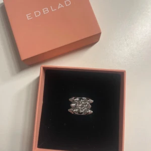 Kan tänka mig byta mot samma fast i guld - Cool och chunky ring från Edblad i blankt silverfärgat metall. Ringen har en bred form med flera små konformade nitar som ger en edgy vibe. Perfekt för dig som gillar att sticka ut med dina accessoarer och vill ha något som syns.