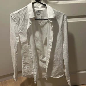 Vit skjorta från Filippa K, storlek 46 - Klassisk vit skjorta från Filippa K i storlek 46. Skjortan har lång ärm, krage och knäppning framtill. Endast använd enstaka gånger så inga hål eller fläckar eller liknande. Dock ej struken pga trasigt strykjärn tyvärr