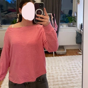 Rosa stickad tröja med offshoulder - Säljer en söt rosa stickad tröja med offshoulder-look och långa ärmar. Tröjan har en avslappnad passform och bred ribbad kant vid halsen.