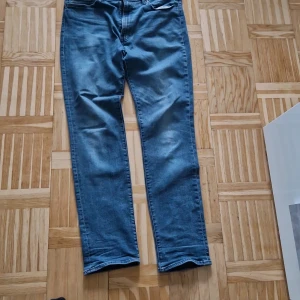 Levi's 511 blå jeans straight fit 38/34 - Säljer ett par klassiska Levi's 511 jeans i blå denim. Modellen har en rak passform med normal midja och fem fickor. Jeansen är tillverkade i bomull och har den ikoniska Levi's Premium-lappen bak. Perfekta till en avslappnad stil.