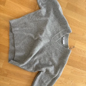 Grå stickad v-ringad tröja från Zara - Mysig grå stickad tröja från Zara med v-ringning och breda ribbade muddar vid hals, ärmslut och nederkant. Perfekt för lager-på-lager och chill vibes. Enkel att matcha med jeans eller kjol.