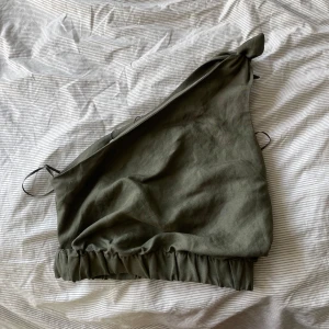 Olivgrön oneshoulder topp med knyt - Snygg olivgrön topp med oneshoulder-design och knytdetalj på axeln. Toppen har en croppad passform och elastisk kant nedtill som ger en cool och avslappnad vibe. Skriv ifall intresserad💞💞