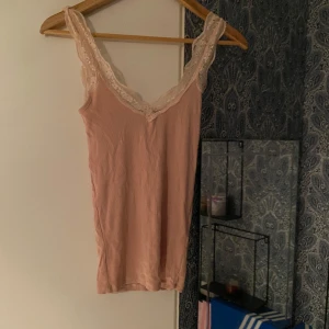 Beige ribbad linnetopp med spets - Supersöt beige linnetopp med ribbad struktur och vacker spetskant längs urringningen och axelbanden. Perfekt att styla med jeans eller kjol för en avslappnad men ändå feminin look.