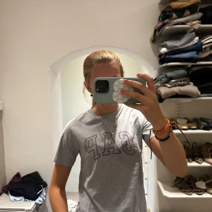 Grå GAP t-shirt med tryck - Säljer en grå t-shirt från GAP med stort tryck över bröstet. Klassisk rund hals och korta ärmar. T-shirten har en loose passform och är gjord i mjuk bomull, perfekt för chill dagar. Enkel och stilren design som funkar till jeans eller shorts.