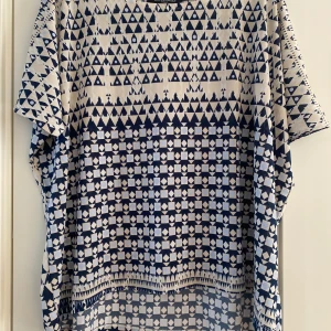 Mönstrad topp från Ilse Jacobsen - Topp från Ilse Jacobsen med kort ärm och loose passform. Den har ett unikt geometriskt mönster i marinblått och vitt, med både trianglar och fyrkanter. Materialet känns mjukt och luftigt, perfekt för varmare dagar. Snygg och modern look som sticker ut.