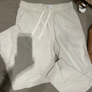 linnebyxor från Zara - Min brors gamla beiga linnebyxor från Zara med avslappnad passform och bred resår i midjan. Byxorna har snörning i midjan och raka ben, perfekta för en chill och stilren look. Lätta och luftiga i materialet, passar grymt till sneakers eller sandaler.