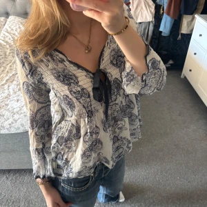 Odd Molly blus med paisleymönster - Supersöt blus från Odd Molly i vitt med marinblått paisleymönster. Blusen har v-ringning med svart knytband, smockad överdel och volangig nederdel. Trekvartsärmar med spetskant ger en romantisk vibe. Perfekt till jeans för en chill men snygg look. Den är så fin verkligen men kommer inte till användning tyvärr så hoppas den kan vara det hos någon annan. Storlek står inte men skulle säga mellan S och M