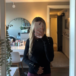 Svart långärmad tröja med knappar - Snygg svart långärmad tröja med guldiga knappar längs ärmsluten. Materialet känns mjukt och stretchigt, vilket gör den skön att bära hela dagen. Hör av dig om du har några frågor! 🫶🏼💕