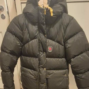 mörkgrön  Fjällräven  - Säljer en mörkgrön dunjacka från Fjällräven 1974 Expedition Series i storlek XS. Jackan har en rejäl huva, gula snören, dragkedja och knappar framtill samt två stora fickor. Perfekt för kalla dagar och riktigt snygg streetstil. Införskaffad förra vintern från butik, och säljer för jag vill ha en annan färg i år. Inga defekter.🩷 skriv vid intresse!