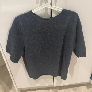 Mörkgrå tröja från Zara - En stilren mörkgrå stickad tröja från Zara med korta ärmar och rund hals. Tröjan har en loose passform och är tillverkad i ett mjukt,  material. Oanvänd! 