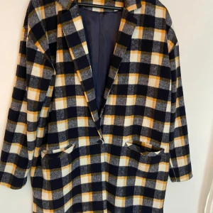 Rutig kappa i ullmix, blå/gul/vit - Snygg rutig kappa i oversized modell med stora fickor och en knapp framtill. Färgerna är mörkblå, gul och vit, vilket ger en cool kontrast. Perfekt för höst och vinter, och materialet känns mjukt och varmt. Passar dig som gillar statement-plagg med retrovibbar.