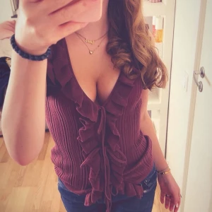 Vinröd topp - Supersnygg vinröd linnetopp med djup v-ringning och volangdetaljer längs hela framsidan. Toppen har knyt framtill och är ribbad i materialet, vilket ger en cool och trendig look. Perfekt att matcha med jeans eller kjol för en stilsäker outfit. Perfekt för hösten!!