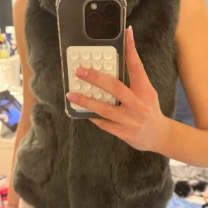 Mörkgrå fluffig pälsväst med huva - Säljer en mörkgrå pälsväst med huva som är supermjuk och har två praktiska fickor framtill. Västen är helt ärmlös och har en snygg, lite oversized look. Perfekt att slänga över en hoodie eller långärmad tröja för extra värme och stil. Passar xs-S 