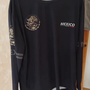 Unik Svart långärmad Mexico-tröja - Svart långärmad tröja med tryck av Mexikos statsvapen och texten 'MEXICO' på bröstet. Tryck även på ena ärmen. Rund halsringning och normal passform. Perfekt för dig som vill visa lite extra kärlek till Mexiko.