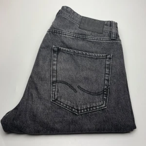 Grå jack & joens jeans  - Snygga grå jeansbyxor i klassisk rak modell med fem fickor och tydliga sömmar. Jeansen har en cool tvättad look och är tillverkade i slitstarkt denimtyg. Perfekta för dig som gillar en stilren och avslappnad vibe.