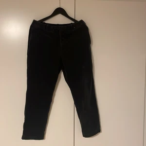 Svarta manchesterbyxor från Uniqlo - Säljer ett par svarta manchesterbyxor från Uniqlo i storlek M. Byxorna har klassisk passform med raka ben, bälteshällor och knappstängning. Materialet är 97% bomull och 3% elastan vilket gör dem både mjuka och stretchiga. Perfekta för dig som gillar stilrena och bekväma byxor.