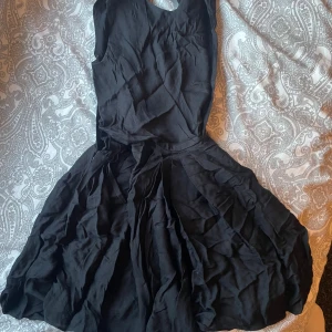 Svart kortklänning från Esther Stenius - Supersnygg svart klänning från Esther Stenius i kort modell. Klänningen har ärmlös design, markerad midja och vidd i kjolen för en riktigt fin siluett. Perfekt för dig som gillar stilrena och klassiska plagg.